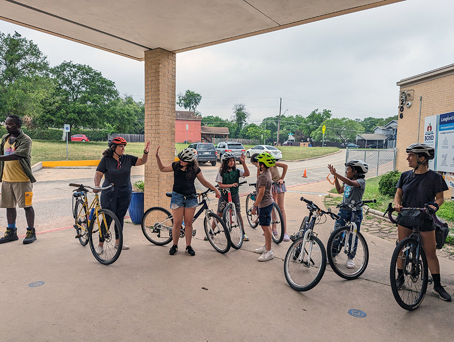 children with bikes high five each other on a covered cement surface