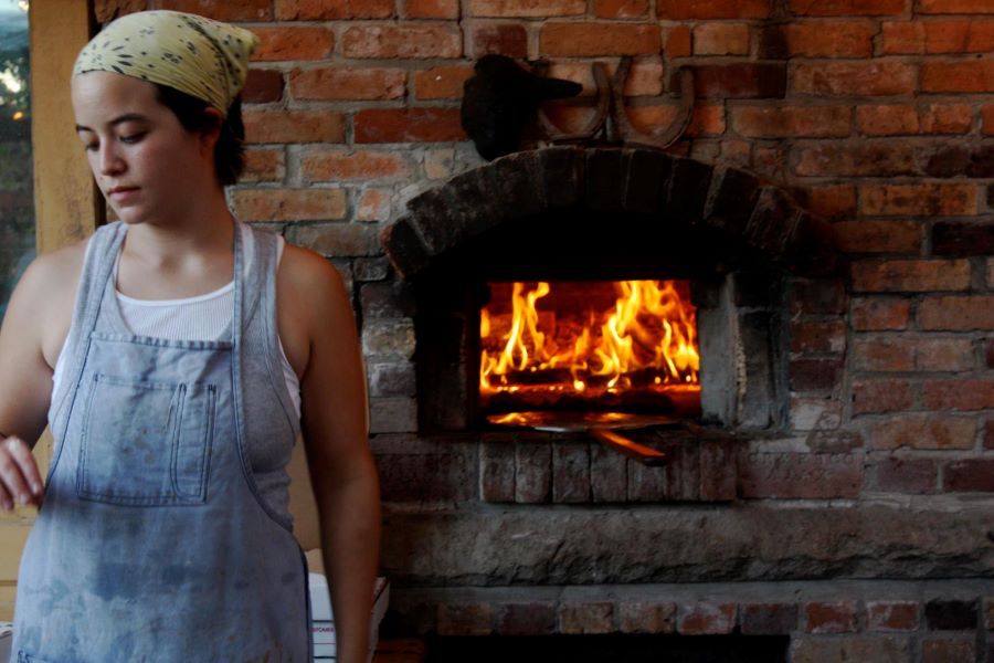 Carmen in a bandanna and apron in front of a pizza oven.