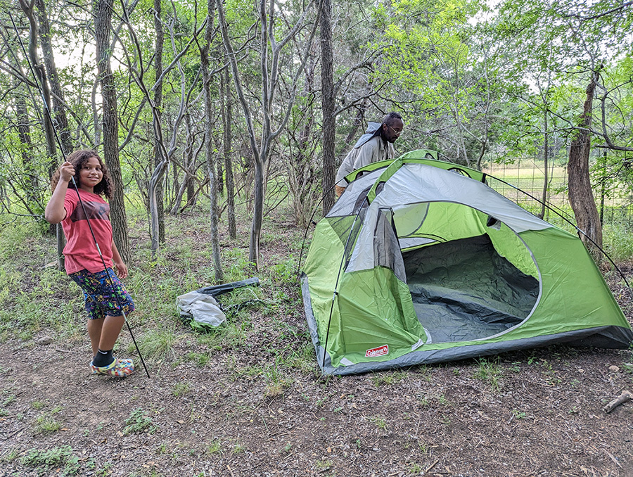 A child holds a tent pole for an adult setting up a tent.